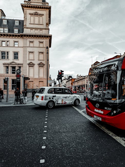 A street scene in Clapham Junction SW4 showing a white taxi and a red and black bus stopped at a traffic light. The area features classic Victorian-style buildings with beige facades, detailed cornices, and multiple windows. The pavement is wet, reflecting the overcast sky, and a few pedestrians wait at the crosswalk. The scene captures everyday urban activity with vehicles, streetlights, and signage visible, highlighting the typical appearance of the Clapham Junction area. Cleaners SW4 offers same day deep cleaning services for residential and commercial spaces, ensuring thorough sanitisation and surface cleaning on various surfaces like floors, counters, and glass in the SW4 area.