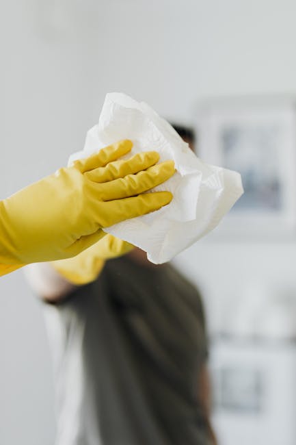 A close-up of a person's gloved hand holding a crumpled white paper towel, with a blurred background that appears to be a kitchen or cleaning area. The surface being cleaned is not visible, but the focus is on the action of wiping or sanitising a surface as part of deep cleaning or surface cleaning processes. The scene highlights hygiene and cleanliness, aligned with the services provided by Cleaners SW4, specialists in domestic and commercial cleaning in Clapham, SW4, as referenced on the page about end of tenancy cleaning.