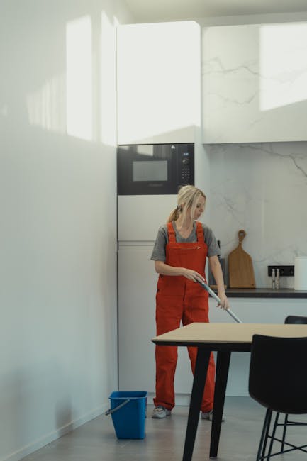 A clean, empty room with light wooden flooring and white walls illuminated by natural light from a window on the right. On the floor, there is a wooden window frame with glass panes laid flat, next to a long, yellow-handled dusting brush. The room appears freshly vacuumed and dusted, with no visible clutter or dust, showcasing proper surface cleaning and maintenance in preparation for end of tenancy, as part of a deep cleaning process by Cleaners SW4. The overall atmosphere is bright and tidy, emphasizing cleanliness and readiness for new occupancy.